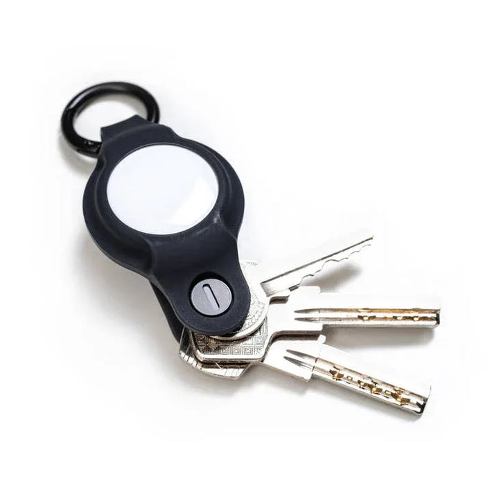 Schlüsselbund mit drei Metallschlüsseln und schwarzem AirTag-Halter auf weißem Hintergrund