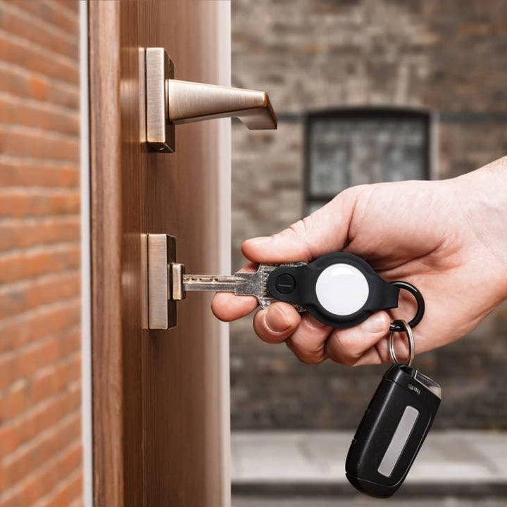 Hand steckt Schlüssel mit Schlüsselanhänger und Autoschlüssel in Haustür, moderner Eingangsbereich